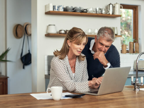 Man and woman reviewing information on a laptop computer on a table in a kitchen with a coffee mug by paperwork