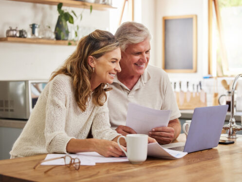 Man and woman reviewing paper work and information on a laptop computer on a table in a lite kitchen